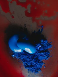 Close-up of vibrant blue pigment powder and glossy cobalt gel resting on a translucent red fluid surface.