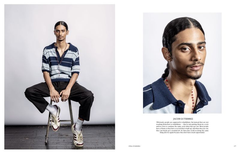 Portrait of a young adult man sitting on a stool wearing a striped shirt, dark pants and sneakers in a photo studio setting.
