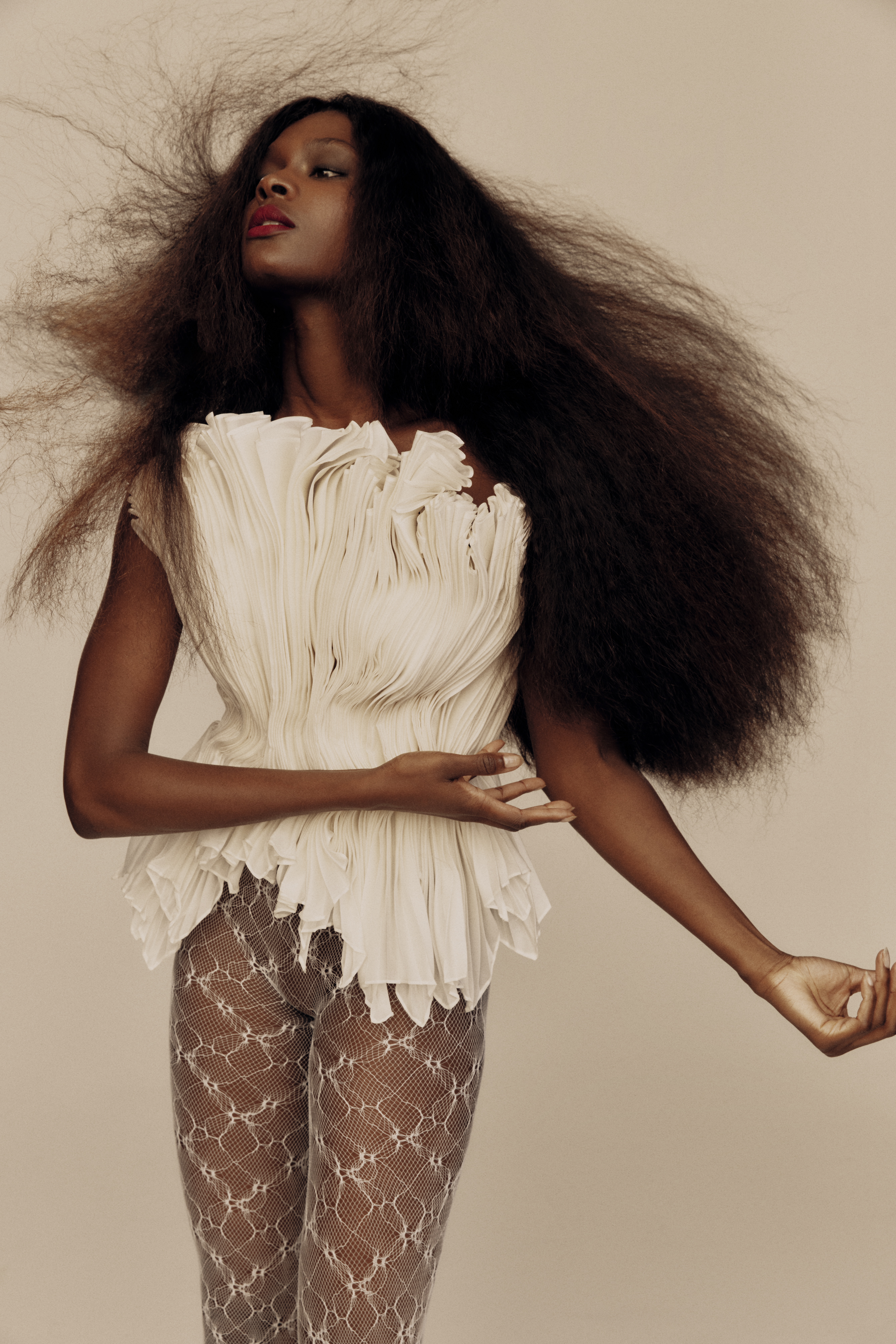 A striking studio portrait features a Black female model with voluminous dark hair, wearing a textured white top and sheer patterned tights.