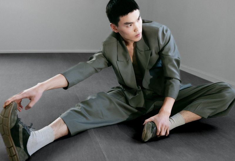 Model Buyant Munkhbat stretching on the floor in an olive green suit and sneakers for a V MAN SEA editorial.
