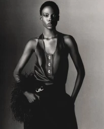 Black and white portrait of model Agel Akol in a sleeveless top and feathered accessory against a studio backdrop.