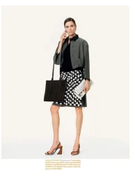 Model Vaiora Stroganoff posing with a phone to her ear, carrying a dark tote bag and newspaper against a white studio background.