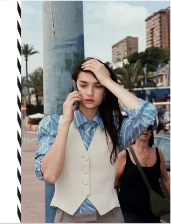 Model leaning against a post in a blue striped shirt and white vest making a phone call outdoors in Benidorm