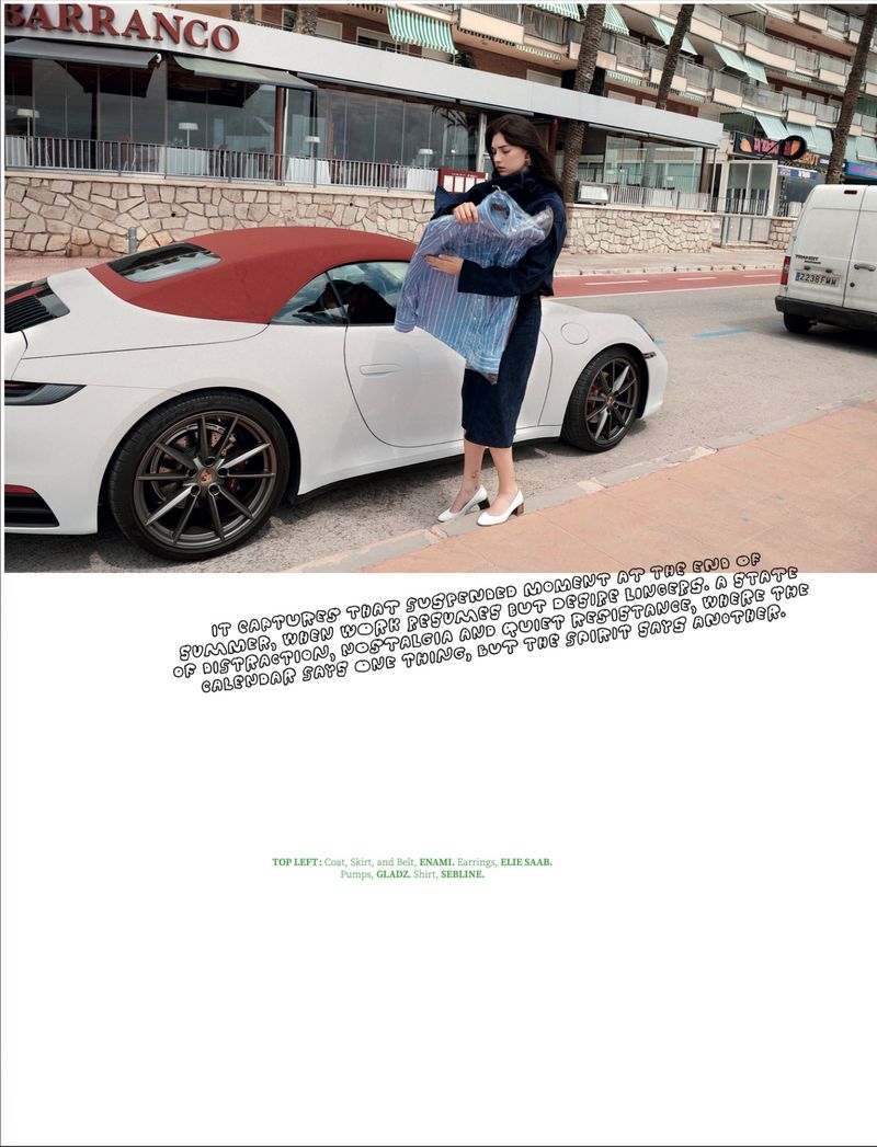 Model standing by a white sports car on a sunny street, holding a wrapped garment for Heatline Magazine editorial