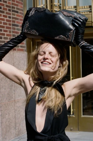 Hanne Gaby Odiele smiling in black leather gloves holding a black handbag above her head outside an entrance.