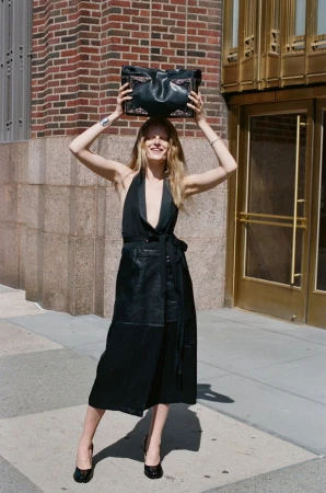 Model Hanne Gaby Odiele balances a black leather bag on her head outside an ornate building in a black halter midi dress.