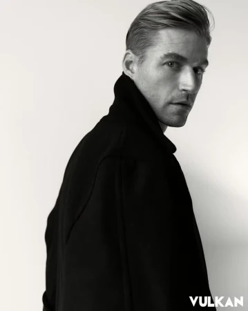 Portrait of a man in a black high-collar jacket against a plain white background for Vulkan Magazine.