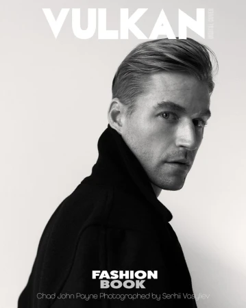 Black and white portrait of Chad John Payne wearing a dark high-collared jacket and looking over his shoulder against a plain backdrop.