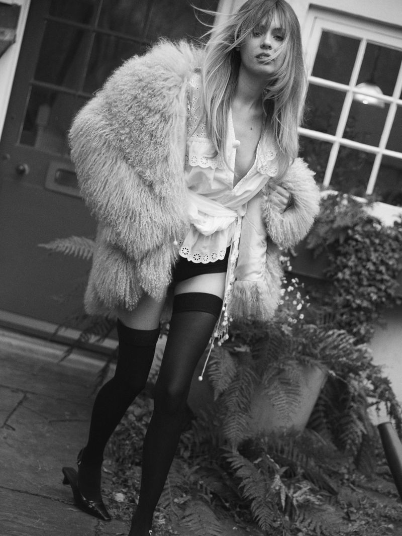 Model Izzy Hawken wearing a shaggy fur coat, lace blouse, and thigh-high stockings outdoors in black and white.