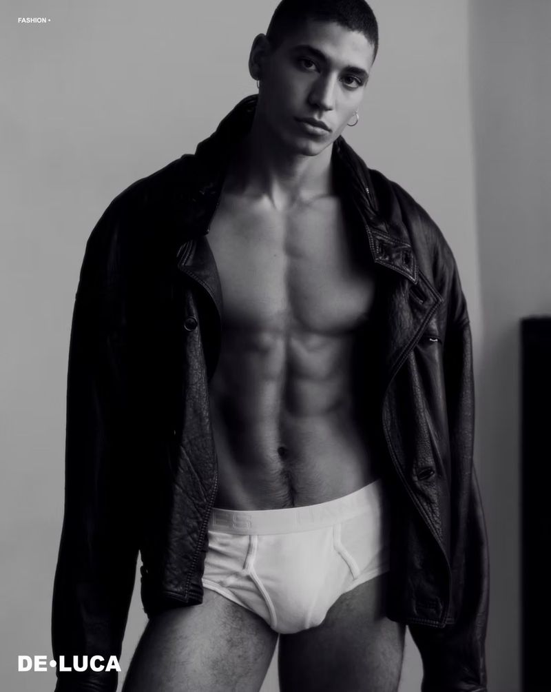 Fashion portrait in black and white of a young adult man wearing a leather jacket and underwear in a studio with soft lighting.