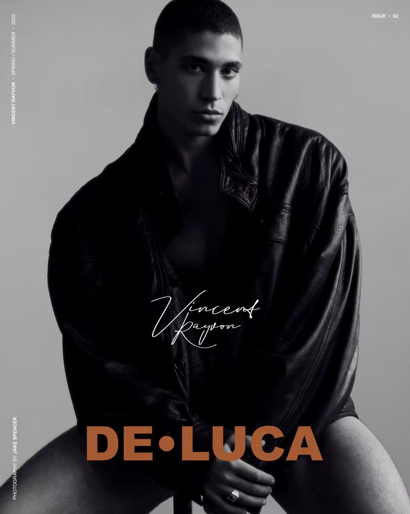 A person in a black jacket poses in a studio setting. The black and white portrait is a fashion editorial with modern typography.