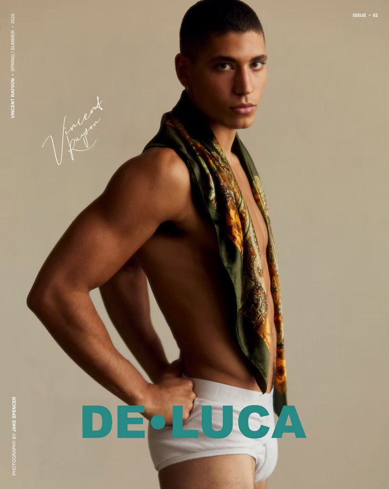 Portrait of a bare-chested adult male with dark hair, a patterned scarf, and white underwear posing in front of a neutral studio backdrop.
