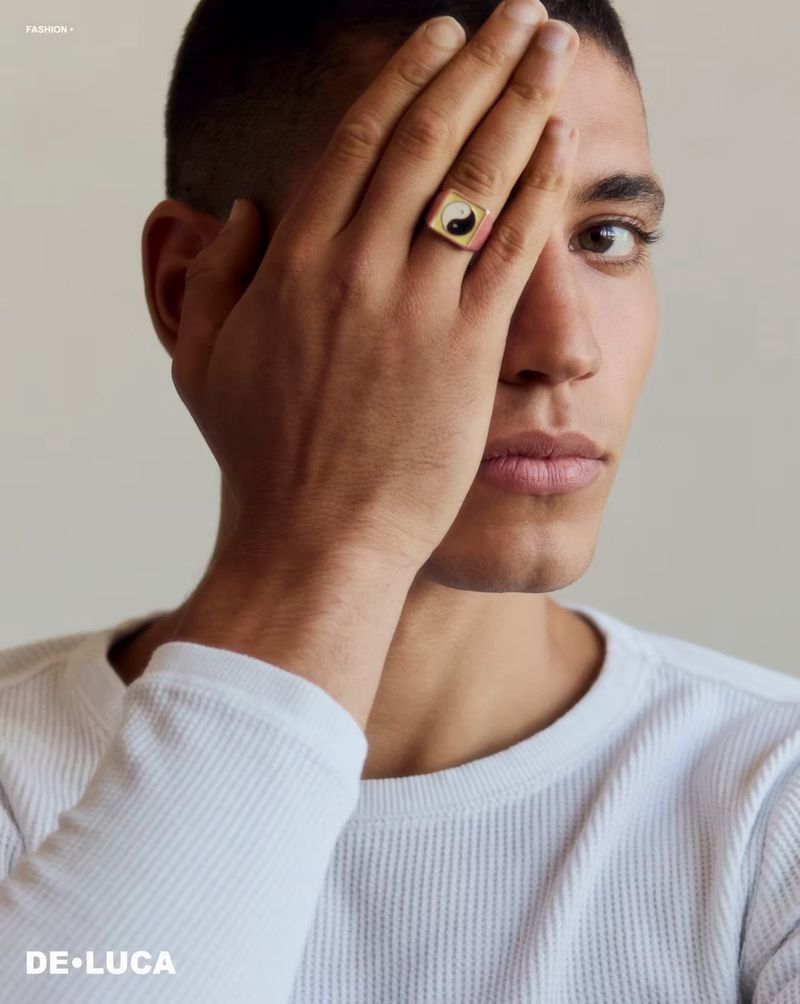 Close-up portrait of a fair-skinned young adult male with dark hair wearing a ring with a yin-yang symbol. Fashion shot on a white background.