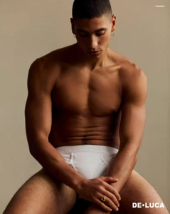 Shirtless male model wearing white underwear seated against a neutral studio background in a fashion portrait for DELUCA Magazine