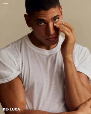 Portrait of a young man wearing a white t-shirt with his hand near his face against a neutral background.
