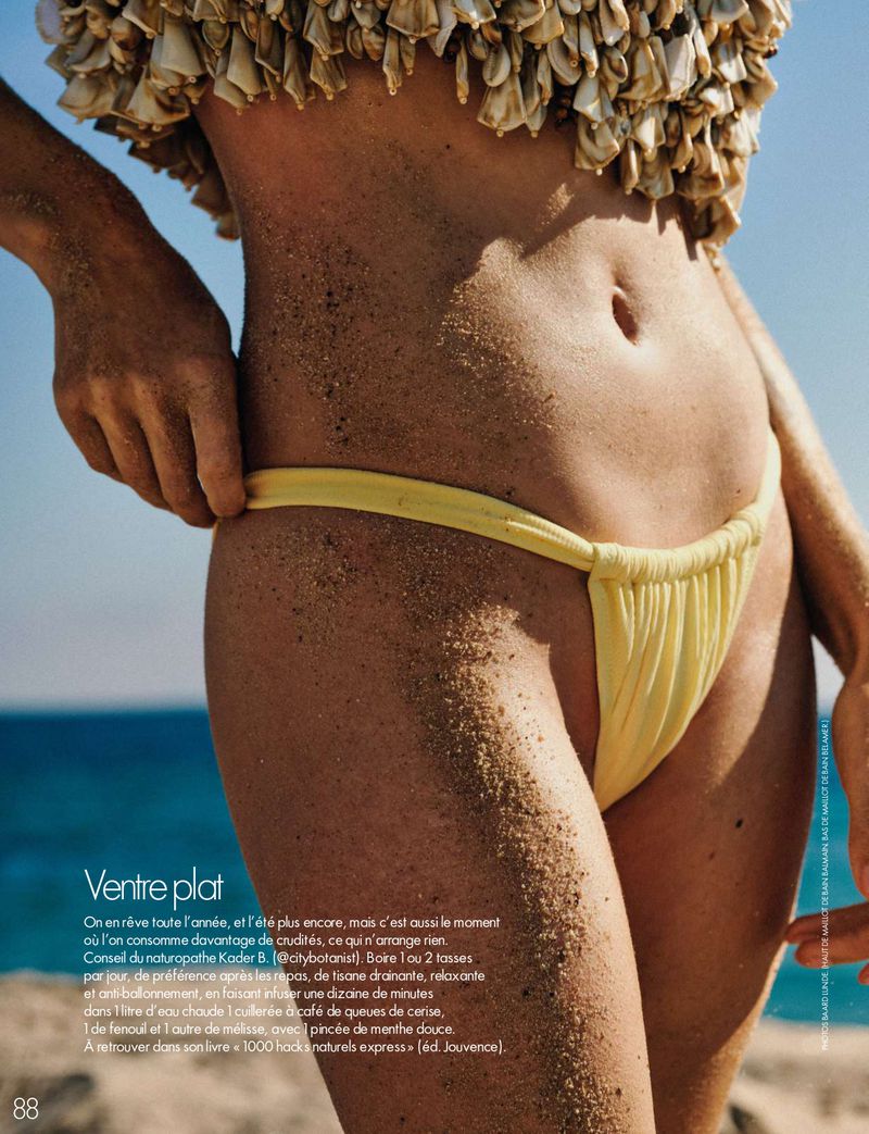 Close-up of a woman's torso covered in sand, wearing a yellow bikini bottom and textured shell top against the ocean.