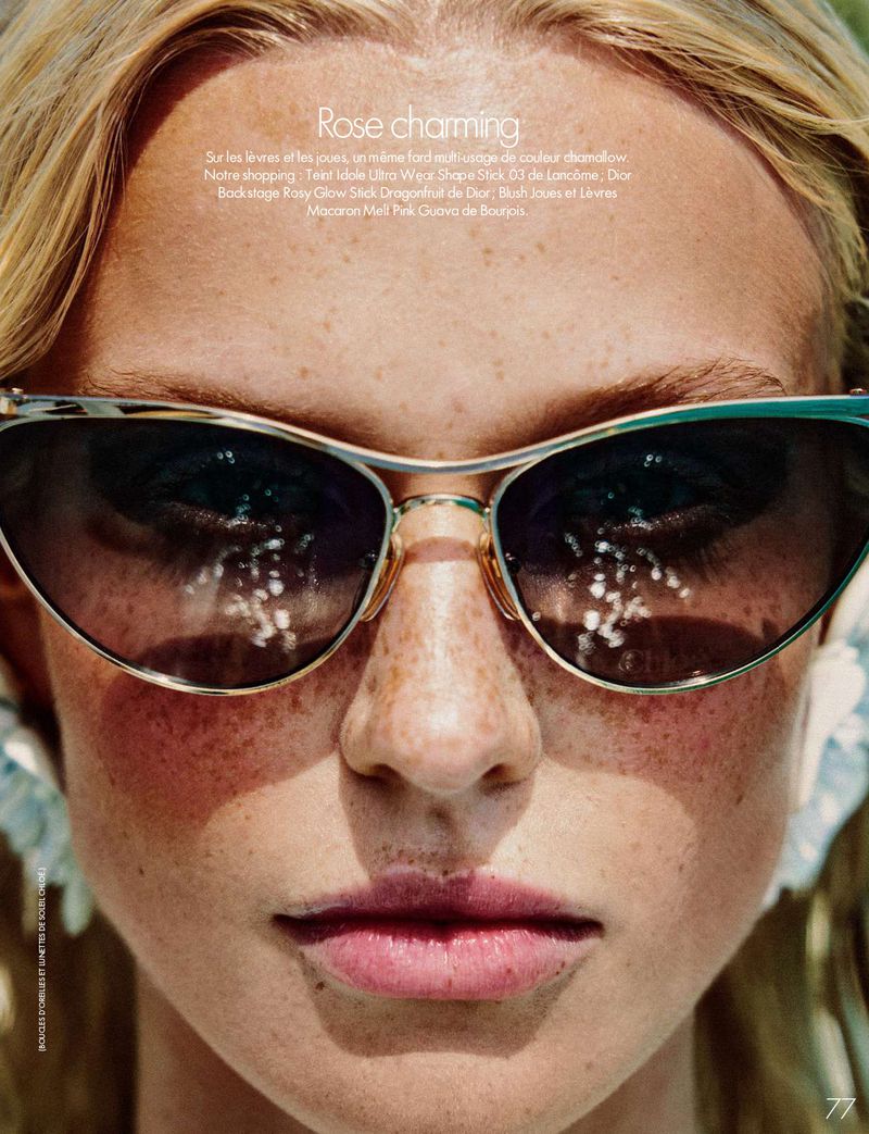 Close-up portrait of a blonde woman with freckles wearing cat-eye sunglasses and pink lipstick.