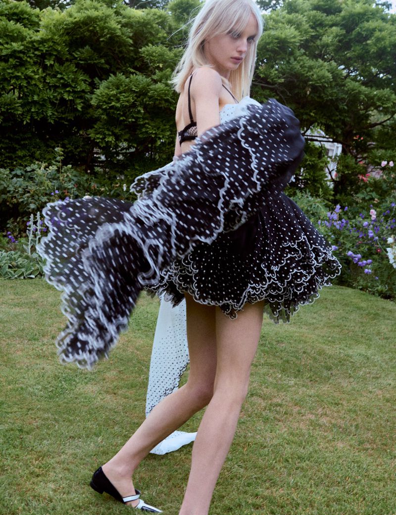 Model Alina Miller in a voluminous black and white ruffled polka dot dress turning dynamically across a lush garden lawn.