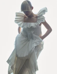 Model Alina Miller in a sculptural white pleated ruffle dress against a bright white background.