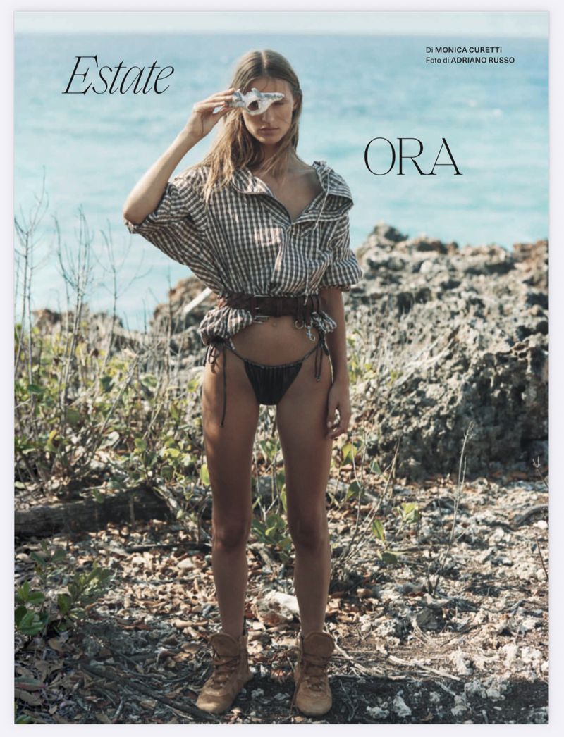 Model Lea Seelenmeyer in a checkered shirt, belted waist, bikini bottoms, and boots on a rocky coast for Elle Italia.