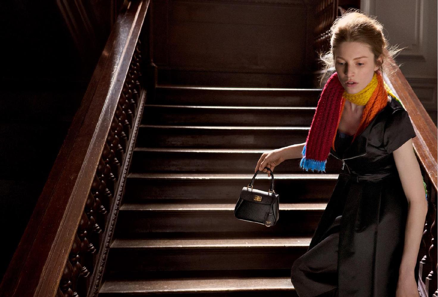 Model wearing black dress and colourful scarf descending wooden staircase holding a black handbag