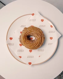 Overhead view of a sugar-dusted cruller pastry on branded Jenny's Bakery wax paper placed on a round white plate.