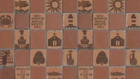 Grid of terracotta ceramic tiles stamped with dark brown nautical and cultural symbols alongside Portuguese phrases.
