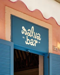 Blue entrance signage for Salva Bar with white cursive lettering above an open doorway with blue louvred shutters on a pink wall.