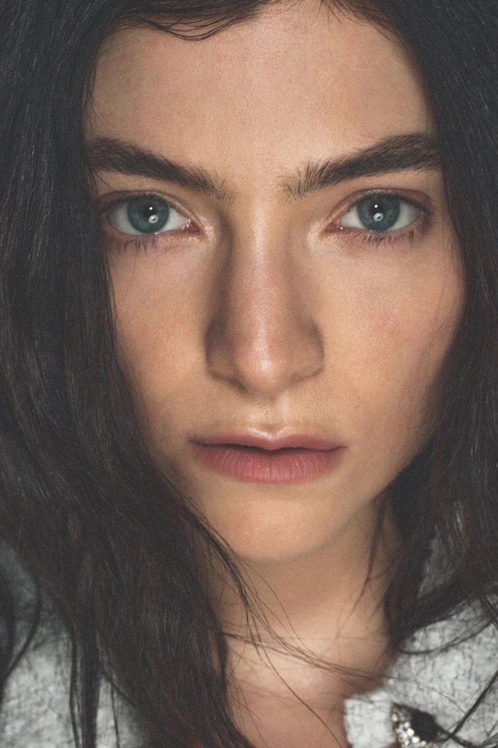 Extreme close-up portrait of singer Lorde looking directly into the camera with dark hair framing her face.