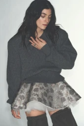 Lorde wearing a grey knit sweater and patterned mini skirt against a white studio background for Vogue Australia