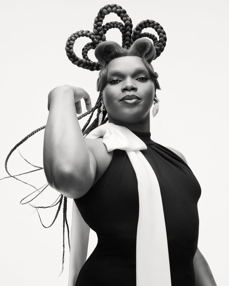 Black and white portrait of a person with sculptural looped braided hair wearing a black sleeveless top with white draped fabric.