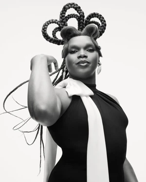 Black and white portrait of a person with sculptural looped braided hair wearing a black sleeveless top with white draped fabric.