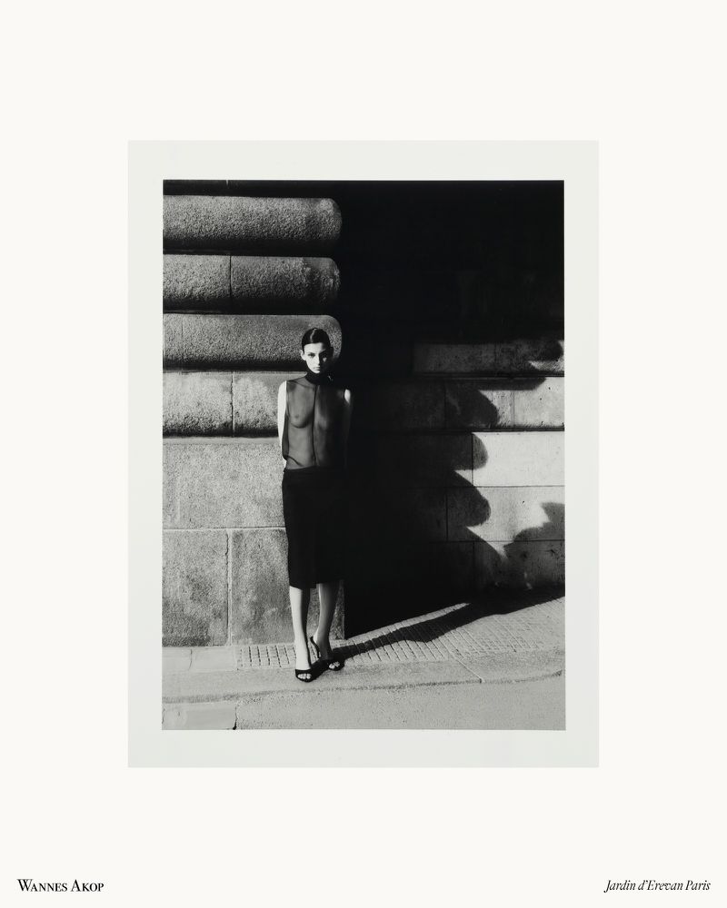 Model Estella Nolan posing in a black sheer top and skirt against a sunlit stone wall with dramatic shadows in Paris.