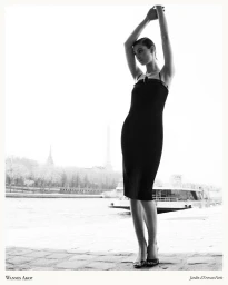 Model Estella Nolan posing in a black sleeveless midi dress on a stone riverbank in Paris for Wannes Akop.
