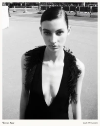 Model Estella Nolan wearing a plunging black feather-trimmed top in a black-and-white outdoor fashion portrait.