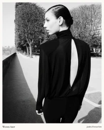 Model wearing a black draped backless top viewed from behind on an outdoor tree-lined walkway in black and white.