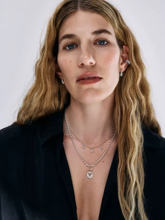 Veronika Heilbrunner wearing layered pendant necklaces, ear cuffs, and an open black shirt against a plain white backdrop.