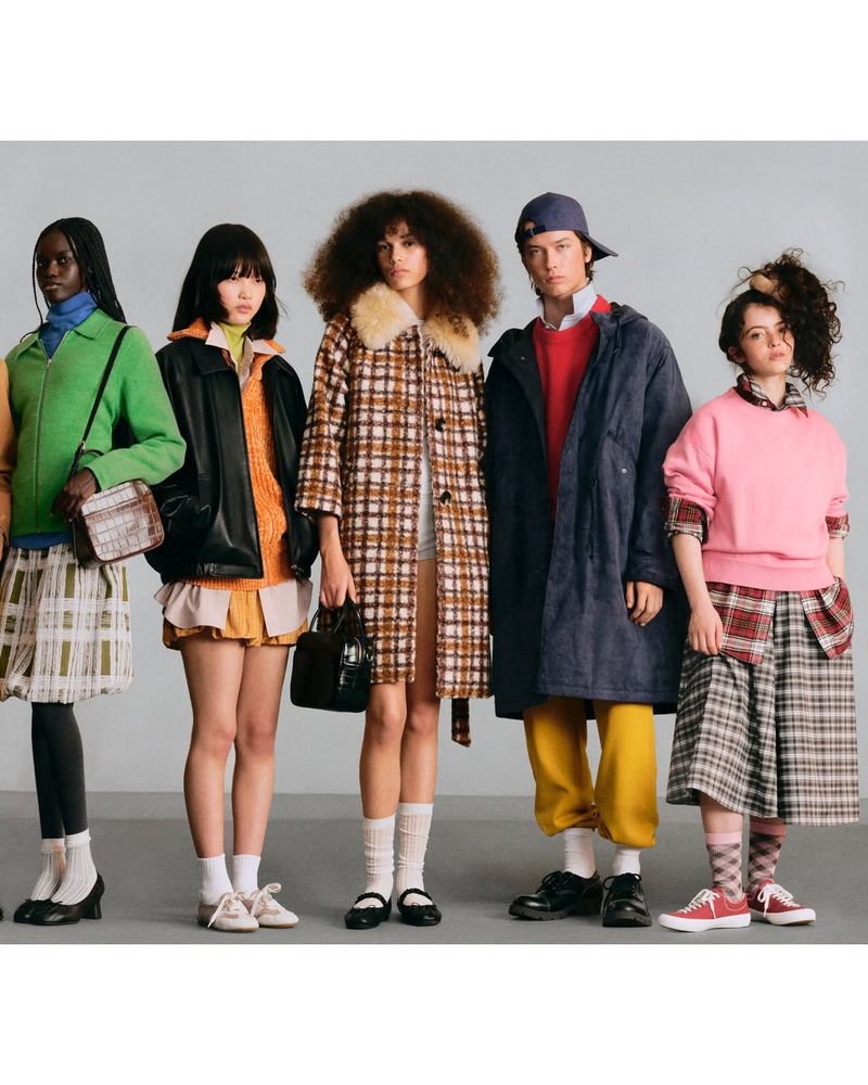 Five fashion models lined up in eclectic layered outfits against a grey studio backdrop.