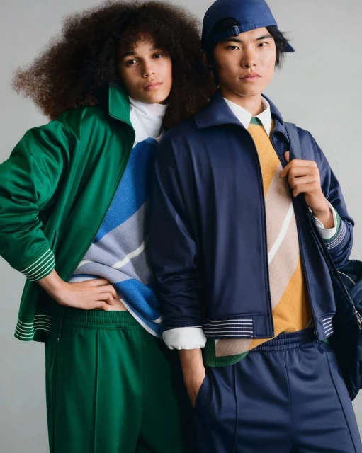 Two models posing in green and navy retro-style tracksuits and patterned knitwear against a neutral studio backdrop.