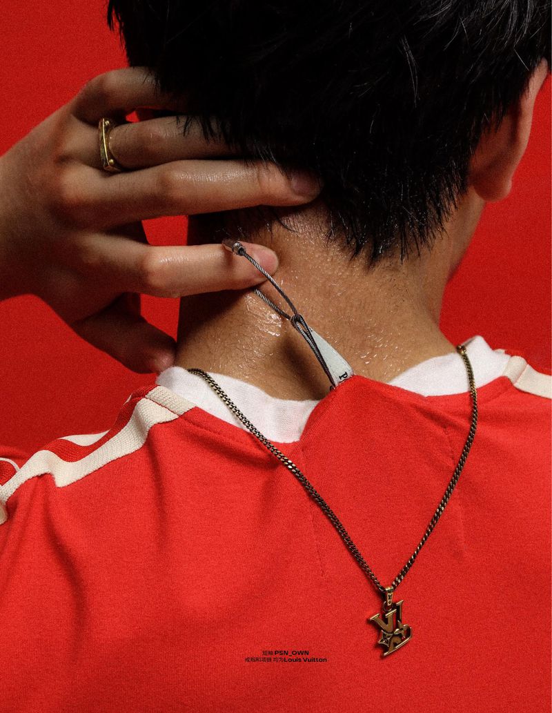 Close-up of a person's neck and back wearing a red t-shirt with white stripes and a gold pendant necklace against a red background.