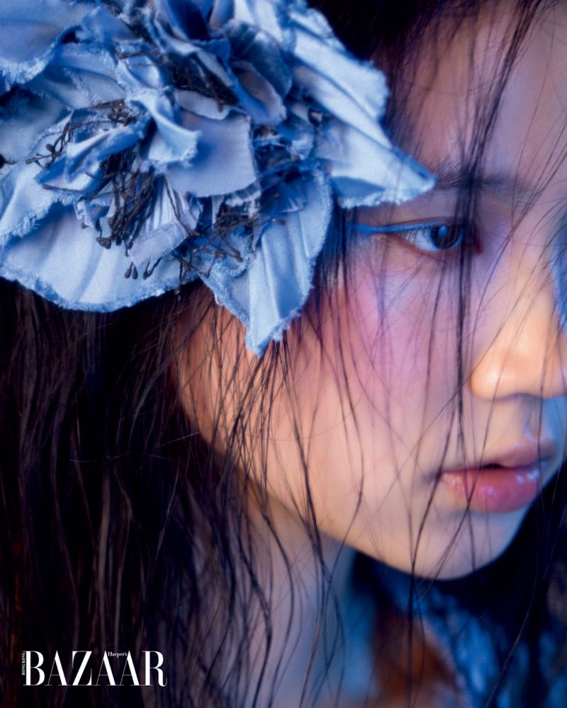 Close-up beauty portrait of a woman wearing a blue fabric flower headpiece with strands of wet hair falling across her face.