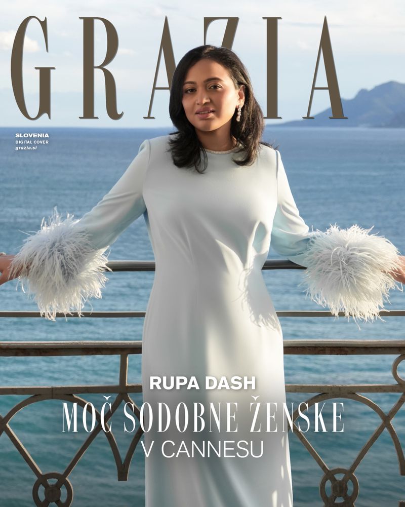 Rupa Dash on a balcony in a pale blue gown with feather cuffs against an ocean view for Grazia Slovenia.