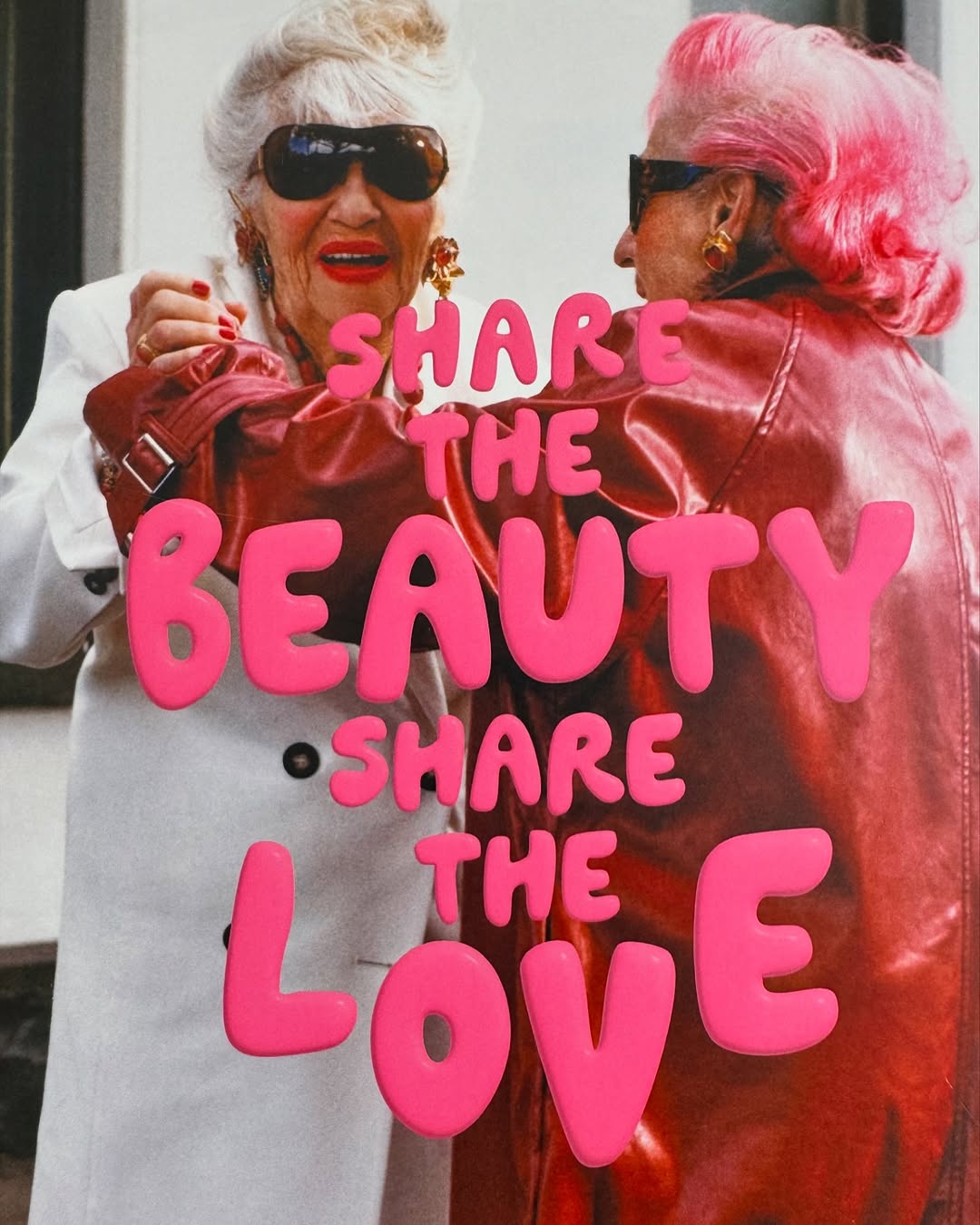 Two elderly women in fashionable outfits pose next to a pink text overlay reading 'Share the Beauty, Share the Love' in a studio setting.