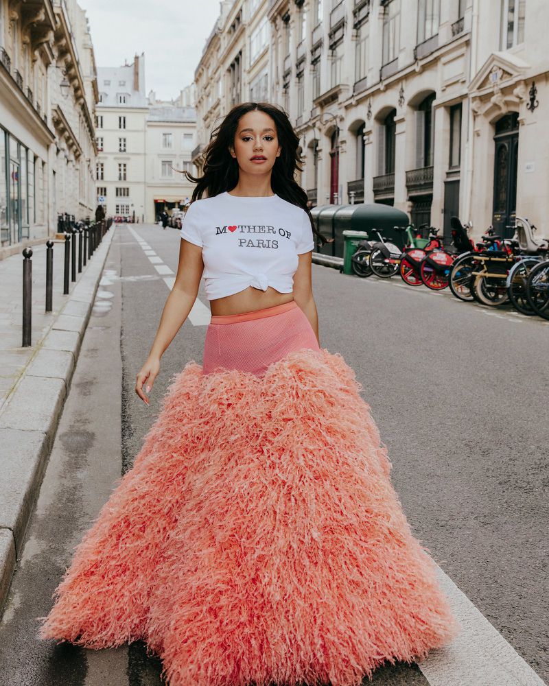 Woman walking on a Parisian street wearing a white t-shirt and a voluminous textured pink skirt for Madame Figaro.