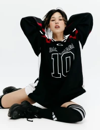 Model seated in an oversized black Balenciaga jersey, knee-high socks, and chunky black sneakers against a white background.