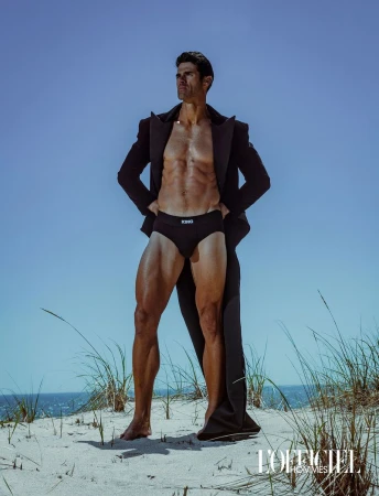 Chad White posing on a sand dune wearing an open black overcoat and black briefs for L'Officiel Hommes Ukraine.