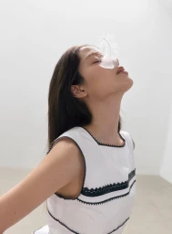 Nana Ou-Yang tilts her head back with a white feather across her face, wearing a white top with black lace trim.