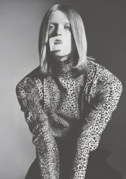 Monochrome portrait of a model wearing a leopard print turtleneck with a lipstick kiss print sticker over their mouth.