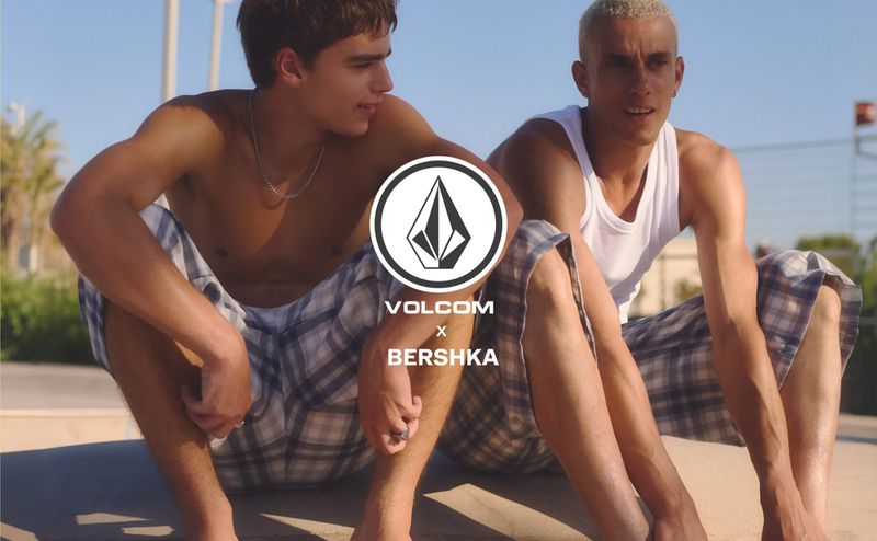 Two young men seated outdoors in skatewear wearing plaid shorts and a white tank top for Volcom x Bershka.