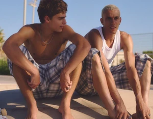 Two young men in plaid shorts seated outdoors in warm sunlight for the Volcom x Bershka campaign.